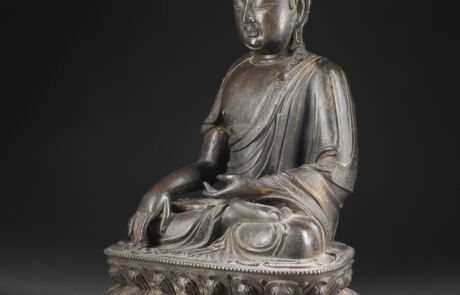 Bronze Buddha sitzt in Meditation auf einem verzierten Sockel. Die Statue ist in einem klassischen Stil mit gefalteten Händen und geschlossenen Augen gefertigt, was Ruhe und Frieden vermittelt. Der Hintergrund ist dunkel, was die Figur betont.