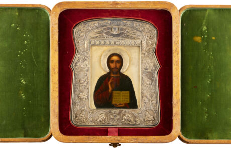 Historische Ikone von Jesus Christus, dargestellt mit Heiligenschein und einem Evangelium in den Händen, eingefasst in einen reich verzierten Silberrahmen. Die Ikone ist in einem aufgeklappten, grünen, samtbeflockten Holzetui platziert, das außen Abnutzungsspuren aufweist.