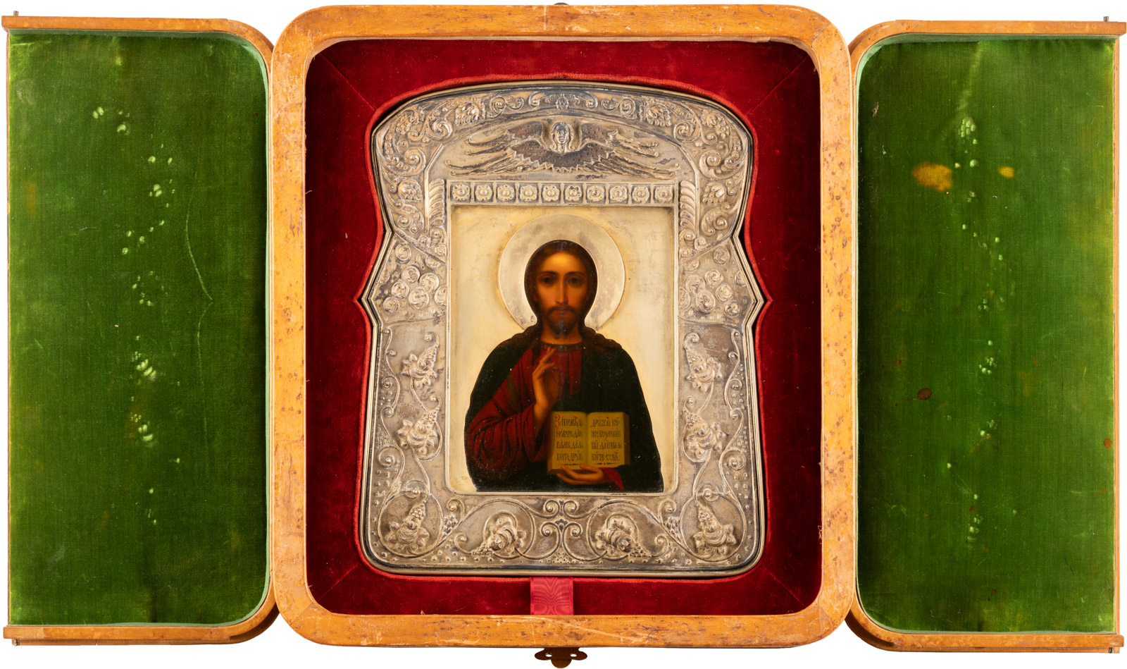 Geöffneter, dreiteiliger tragbarer Altar, zeigend ein mittiges, eingerahmtes Heiligenbild. Im Zentrum, auf einem kleinen Podest, steht ein detailliert gemaltes Ikonengemälde eines Heiligen mit einem langen braunen Haar und Bart, der eine dunkelrote Tunika trägt und seine rechte Hand zum Segen erhebt.