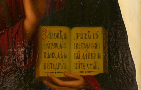 Nahaufnahme eines alten Gemäldes, das die Hände einer Person zeigt, die ein aufgeschlagenes Buch mit kyrillischen Texten hält. Die Seite des Buches ist detailliert sichtbar, und die Textur des Buches sowie die Falten in den roten Gewändern der Person sind deutlich erkennbar.