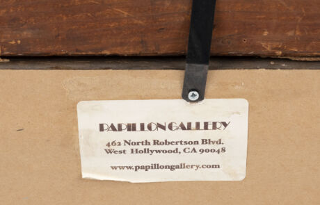 Nahaufnahme eines weißen Etiketts von der Papillon Gallery, das mit einer Metallschraube an der Rückseite eines Kunstwerks befestigt ist. Das Etikett enthält die Adresse "462 North Robertson Blvd., West Hollywood, CA 90048" und die Website "www.papillongallery.com".