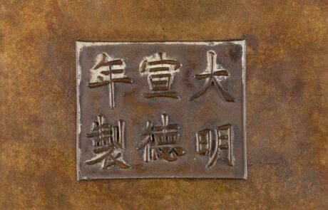 Ein quadratisches Metallrelief mit eingravierten chinesischen Schriftzeichen auf einem rötlich-braunen, texturierten Hintergrund. Das Relief zeichnet sich durch seine klaren, erhabenen Linien aus und die Zeichen sind traditionell gestaltet, was auf einen kunstvollen oder historischen Kontext hinweist.