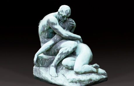 A sculpture depicts two human figures in a close embrace, rendered in muted green and blue tones. The sculpture depicts a visible, emotional moment between the two figures as they sit on a rocky surface. The artwork could have come from an art auction and displays fine details in the depiction of the human.