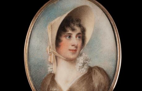 This image shows a portrait of a woman from an earlier era, set in an oval, metallic frame. The person depicted wears a large, light-colored cap and a dark brown dress with a plunging neckline and white lace collar. Her gaze appears thoughtful, and she has slight blushes on her cheeks.