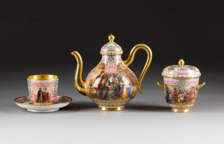 Antikes Teeservice mit kunstvoll bemalter Kanne, Tasse und Zuckerdose auf grauem Hintergrund, präsentiert bei einer Kunstauktion.