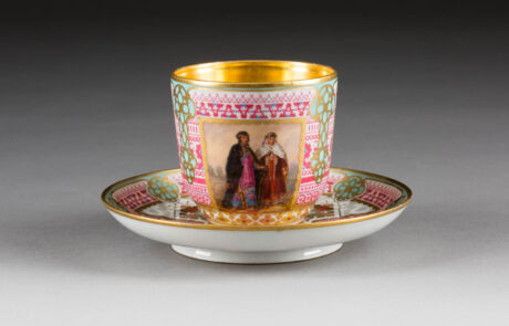 Antike verzierte Teetasse mit Untertasse, bemalt mit Figuren und geometrischen Mustern, präsentiert auf einer Kunstauktion.