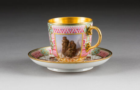 Antike Porzellantasse mit Untertasse, dekoriert mit historischer Szene und Verzierungen, präsentiert bei Hargesheimer Kunstauktion.