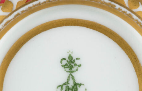 Nahaufnahme eines historischen Porzellantellers mit grünem Blumendekor und Goldrand bei einer Kunstauktion.