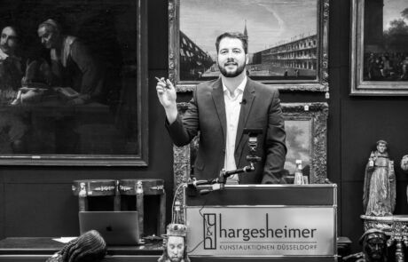Auktionator bei Hargesheimer präsentiert historische Kunstwerke und Sammlerstücke.