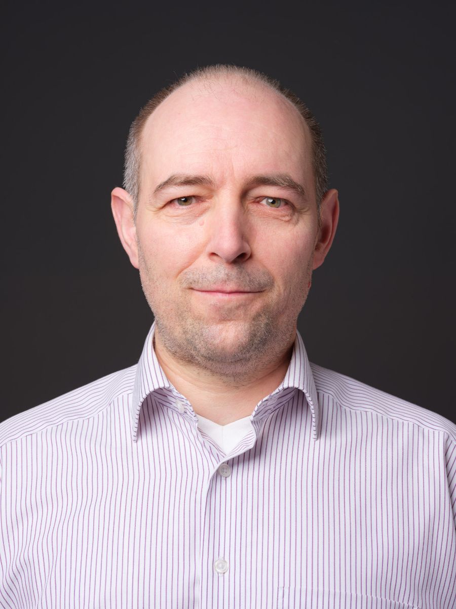 Porträtfoto eines Mannes mittleren Alters in einem gestreiften Hemd vor einem dunklen Hintergrund.