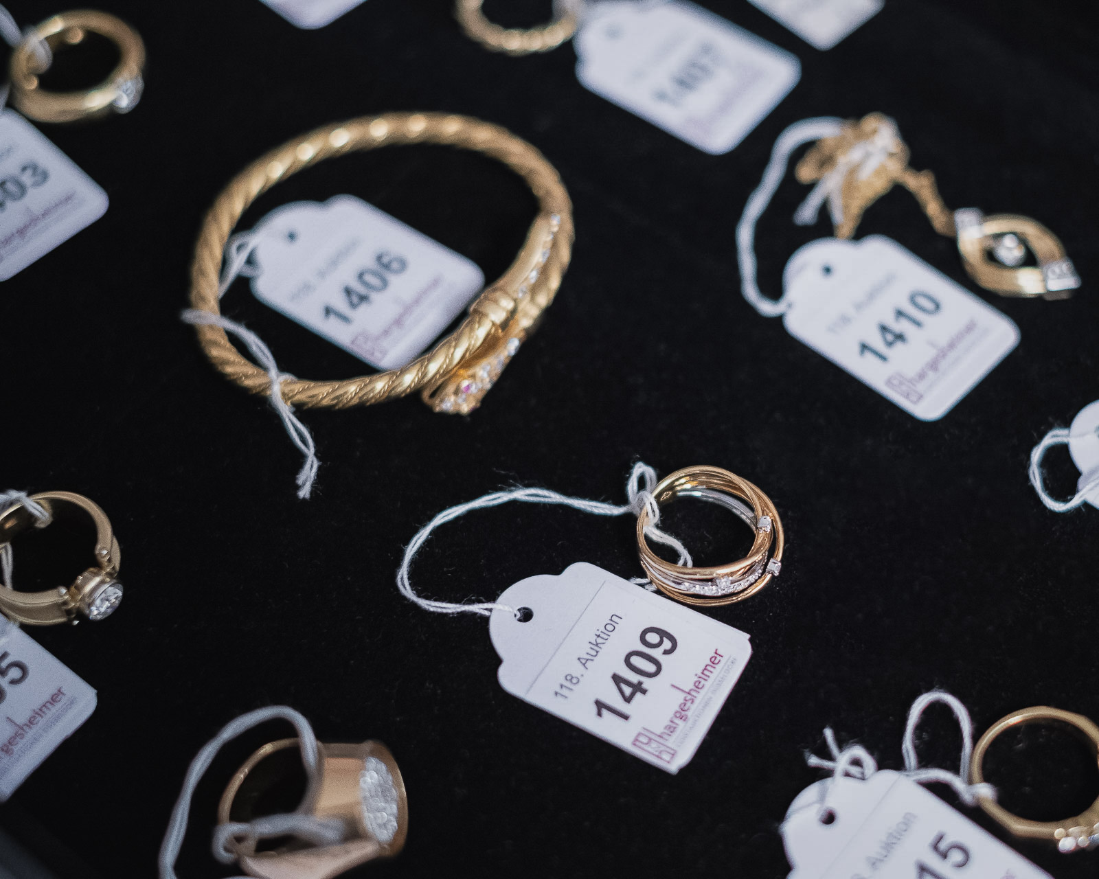 Verschiedene Schmuckstücke auf schwarzem Samt, darunter Ringe und ein Armband, alle mit Anhängeretiketten zur Auktion nummeriert.