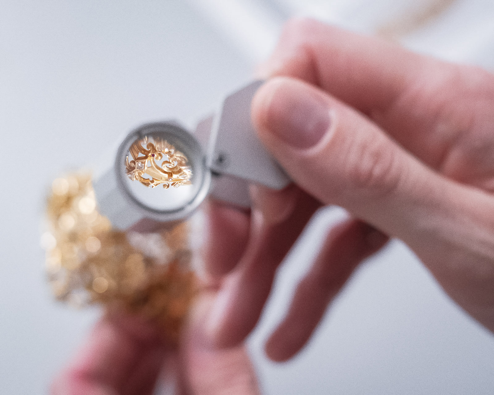 Detailaufnahme einer vergrößerten Ansicht eines kleinen, goldenen Objekts durch eine Lupe, gehalten von einer Person in unscharfem Hintergrund.