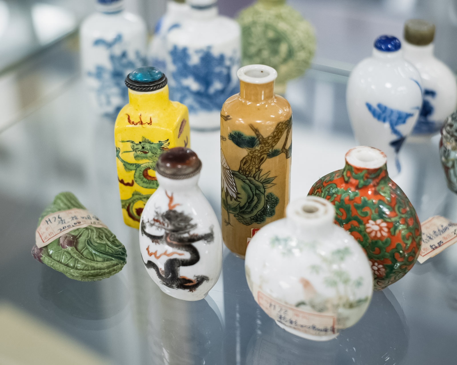 Sammlung von asiatischen Porzellanvasen und -flaschen mit verschiedenen Mustern und Farben, inklusive Drachen und Blumendekorationen, ausgestellt auf einer Glasvitrine.