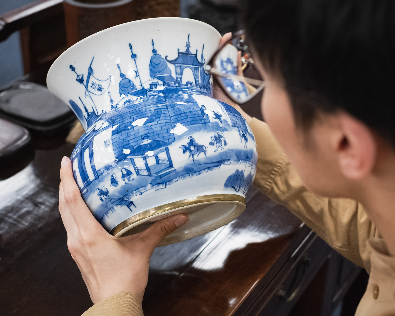 Person betrachtet sorgfältig eine große asiatische Vase mit blau-weißen Mustern, die traditionelle Szenen und Architekturen zeigt.