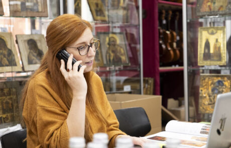 Frau telefoniert im Auktionshaus umgeben von historischen Kunstwerken und Sammlerstücken.