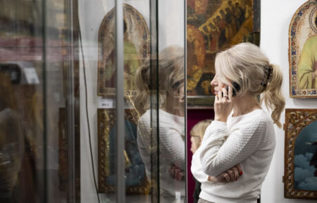 Frau telefoniert neben Vitrine mit historischen Kunstwerken bei einer Kunstauktion.