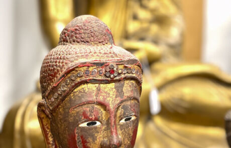 Nahaufnahme einer antiken Skulptur mit roter Bemalung bei einer Kunstauktion, unscharfer Hintergrund mit weiterer Skulptur.