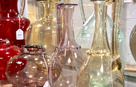 Verschiedene dekorative Glasvasen mit farbigen Akzenten auf einer beleuchteten Auktionstheke.