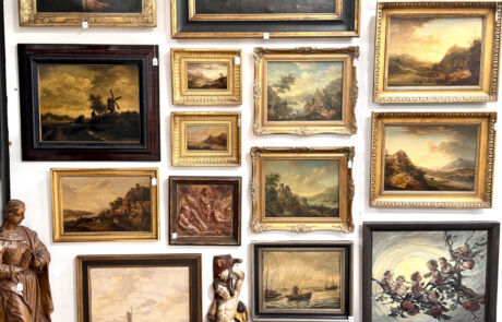 Wand mit diversen gerahmten historischen Gemälden und Skulpturen bei einer Kunstauktion.