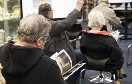 Kunstauktionsbesucher bieten aktiv in einem Auktionshaus mit musealen Sammlerstücken.