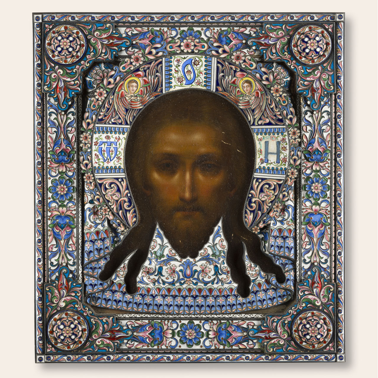 Russische Ikone mit dem Gesicht Christi, umgeben von einem aufwendig verzierten Rahmen mit floralen Mustern und Engelssymbolen in leuchtenden Farben.