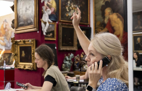 Frau hebt bei Kunstauktion von Hargesheimer Gebot, umgeben von historischen Kunstwerken und Skulpturen.