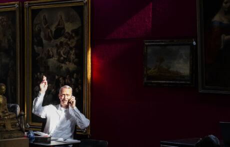 Auktionator führt Kunstauktion in einem Saal mit historischen Gemälden durch.